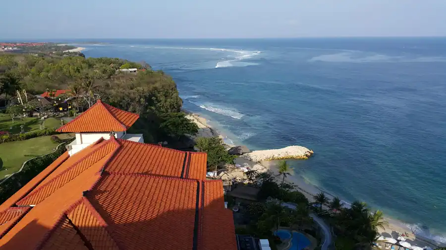 A stunning aerial view of a Bali coastal resort with red roofs and clear ocean waves.