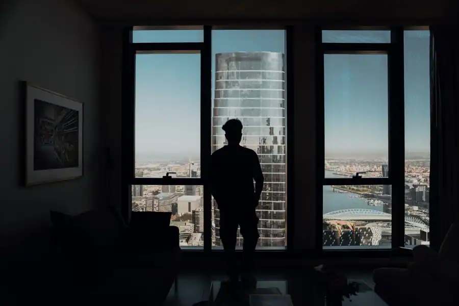 Silhouette of a man standing indoors, gazing at Melbourne's skyline from a high-rise building.