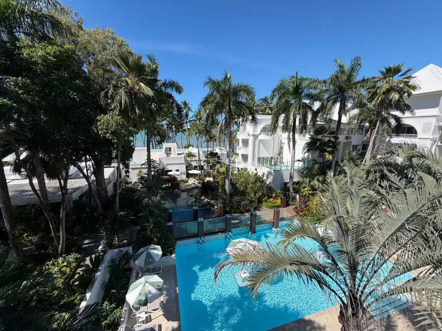Aerial view of a tropical resort pool area with palm trees and ocean view.